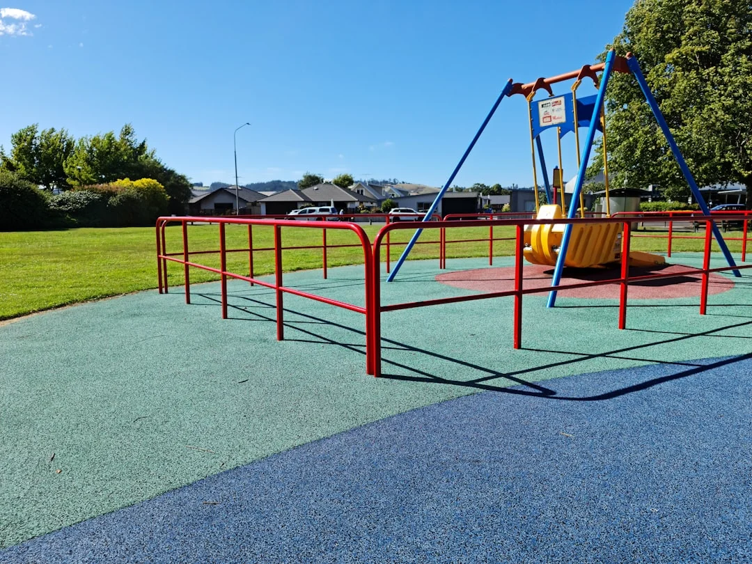 Two young children laughing on a cedar swing set with a slide in a sunny suburban backyard, mulch safety surface visible underneath